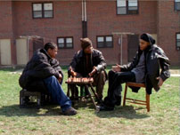 Fig. 9. The Wire (2002-2008). A shot from the low-rises in season 1: the series features many exterior shots but the characters are often ‘closed in’ by buildings. The windows of the tenants appear to look down at D’Angelo (Larry Gilliard Jr.) and his crew like a set of eyes: Someone is always watching… and listening.